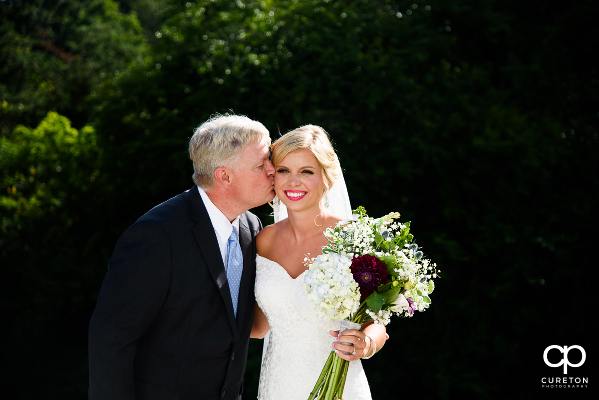 Bride's father kissing her on the cheek before walking her down the aisle.