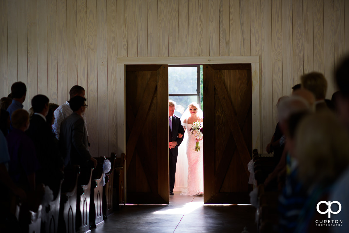 Barn doors opening at the chapel at Chestnut Ridge to reveal the bride and her father at the wedding ceremony.