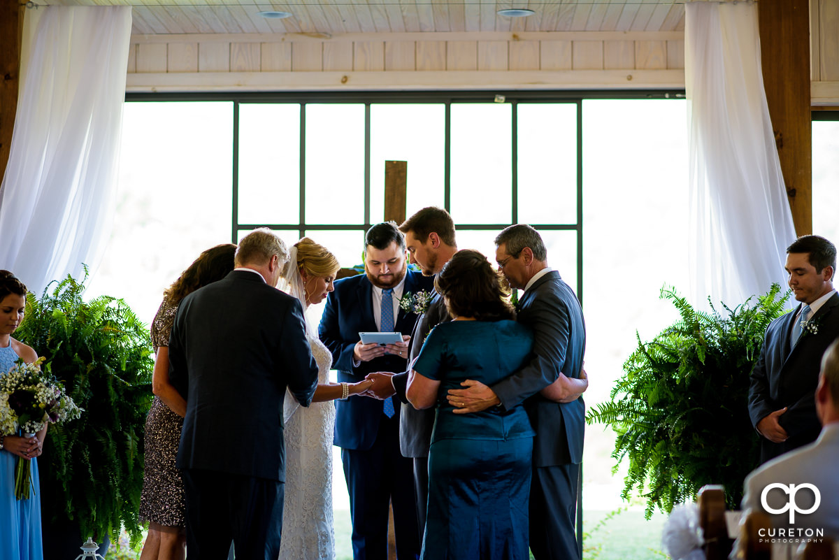 The couple is surrounded by their parents praying over them during the wedding ceremony.