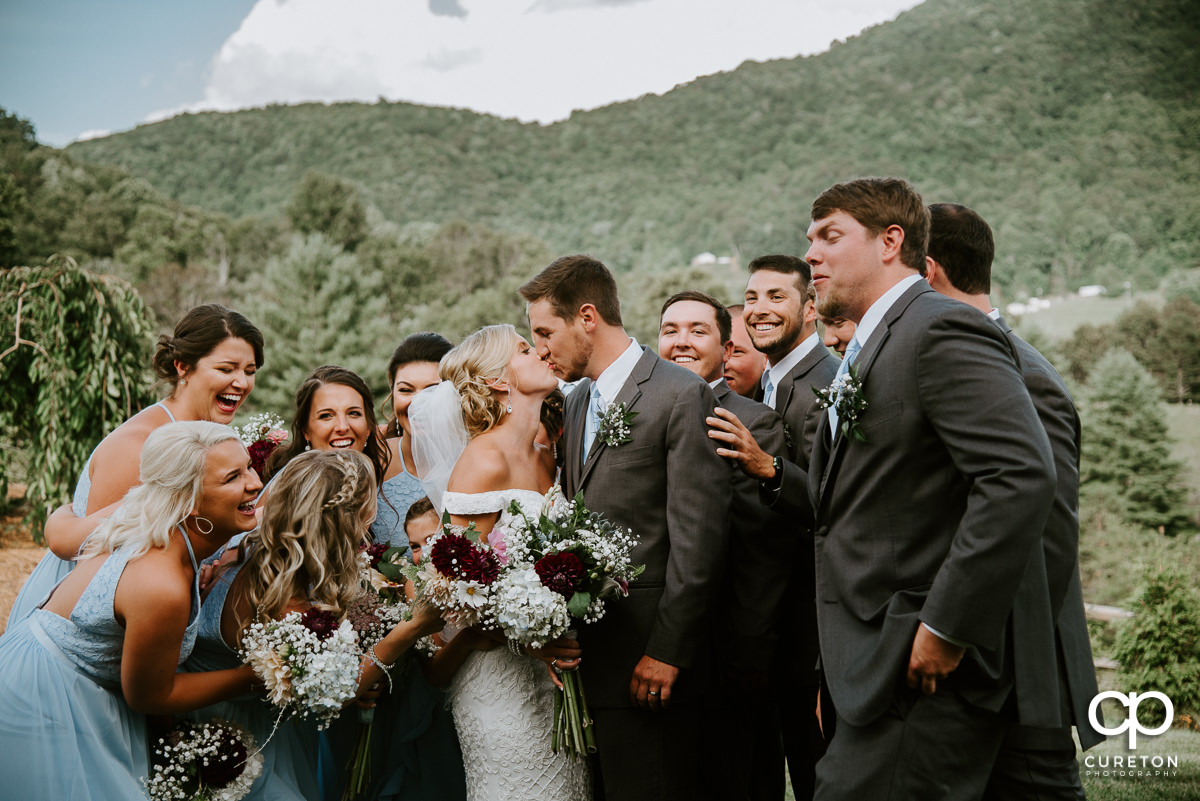 Bride and groom kissing in front of a mountain as the wedding party all hugs them after their wedding at Chestnut Ridge in Canton,NC.