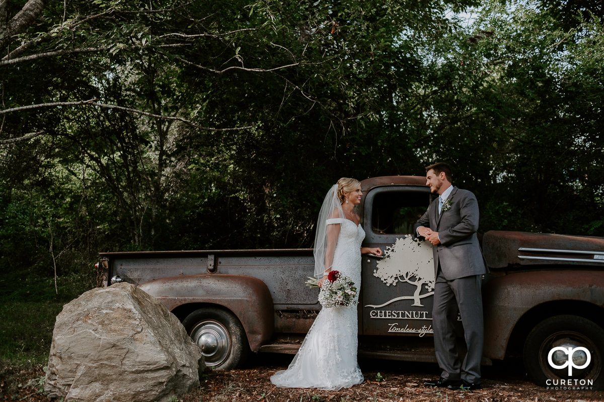 Bride and groom leaning on a vintage pickup truck.