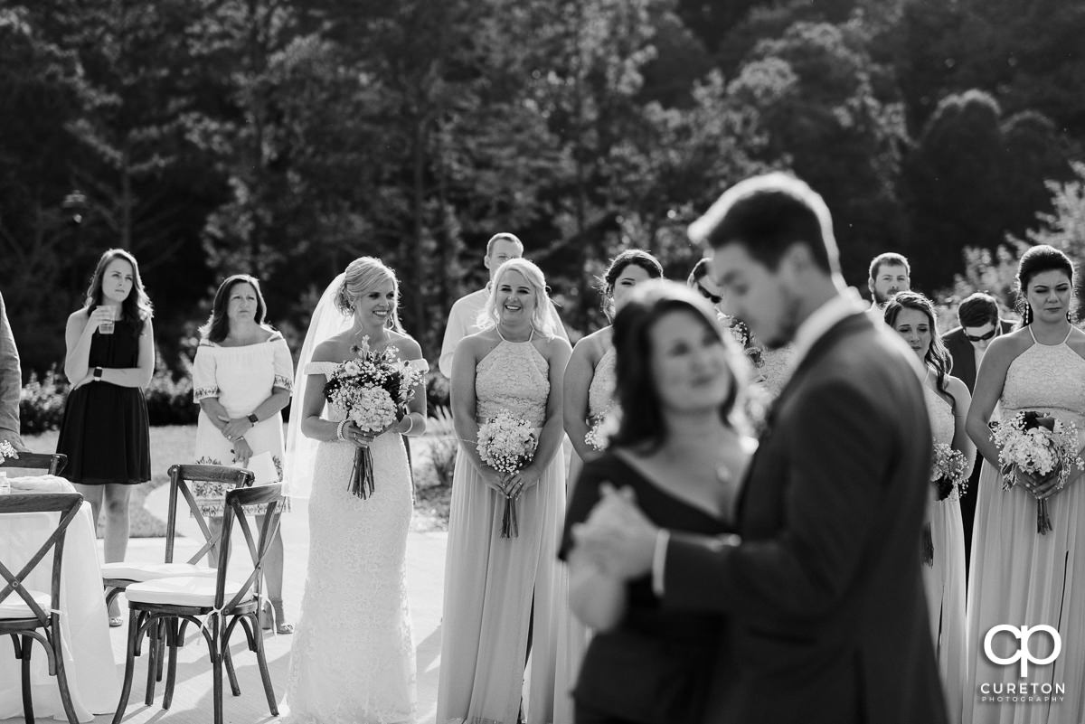 Bride looks on as the groom dances with his mother.