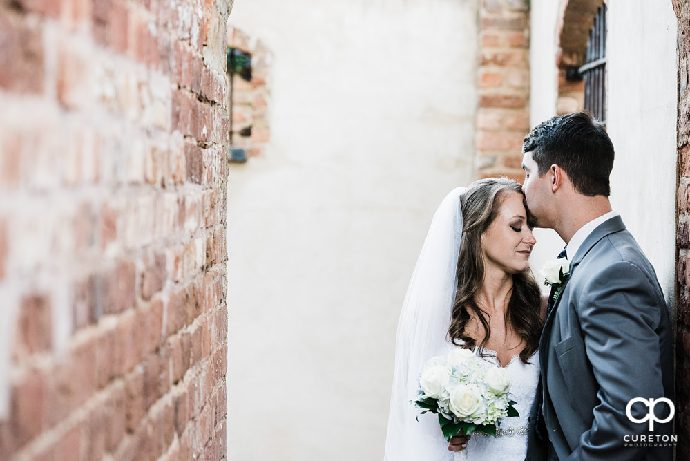 Groom kissing bride on her forehead.
