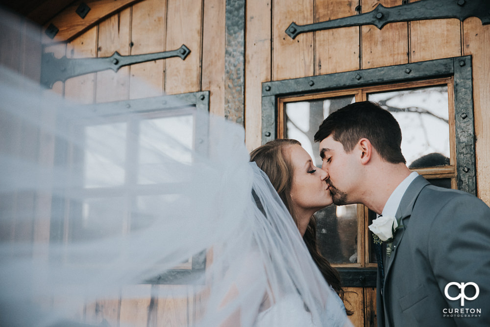 Bride and groom kissing with the veil blowing in the wind.