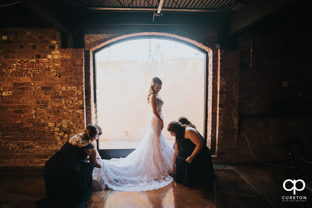Bridesmaids helping bride get ready in a huge window.