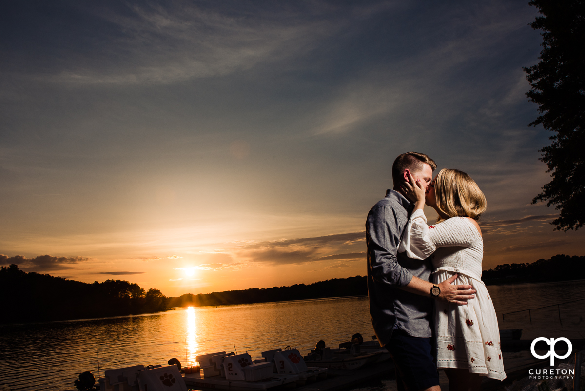 Future Bride an Groom kissing at sunset by the lake during a Clemson engagement session.