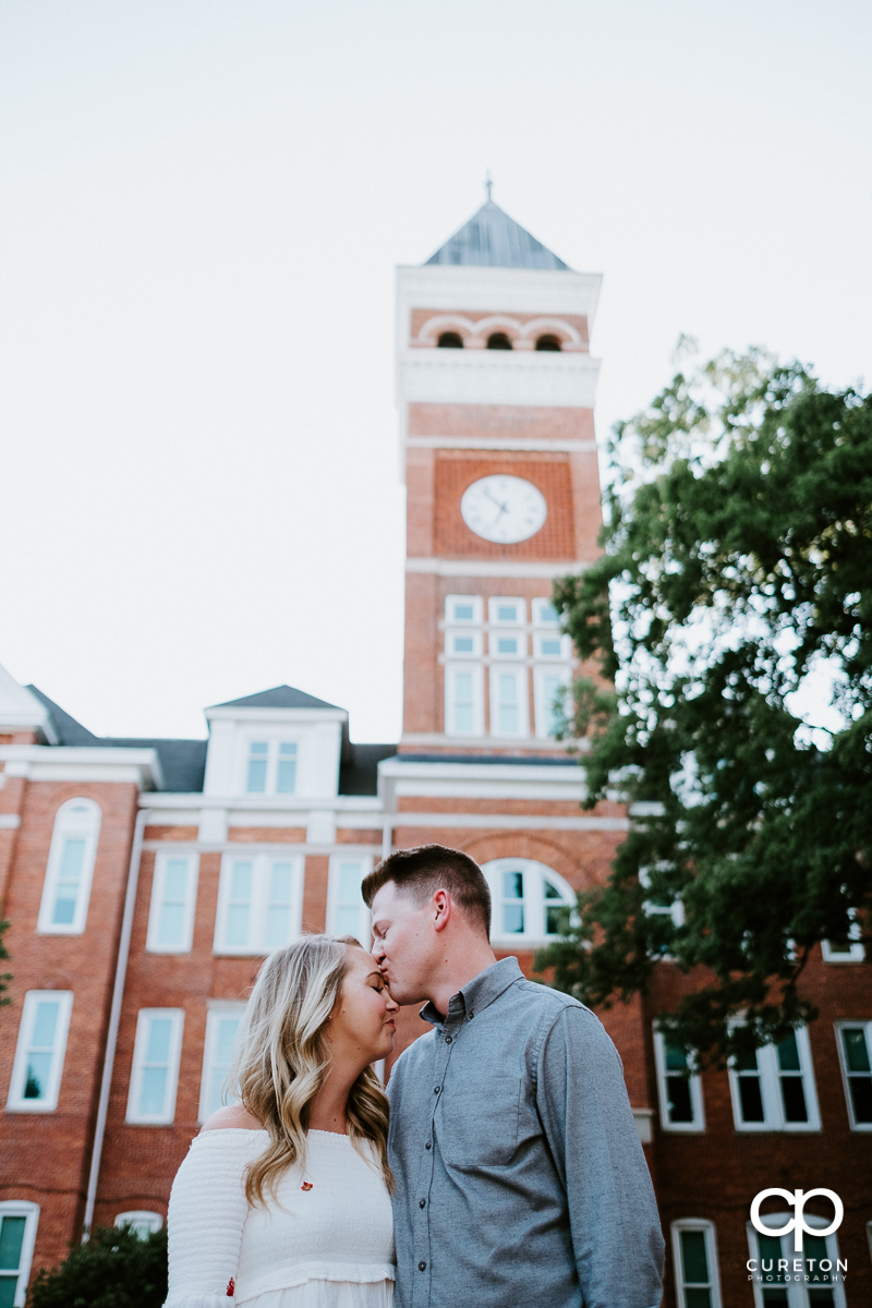 Man kissing his fiancee on the forehead in front of Tillman Hall.