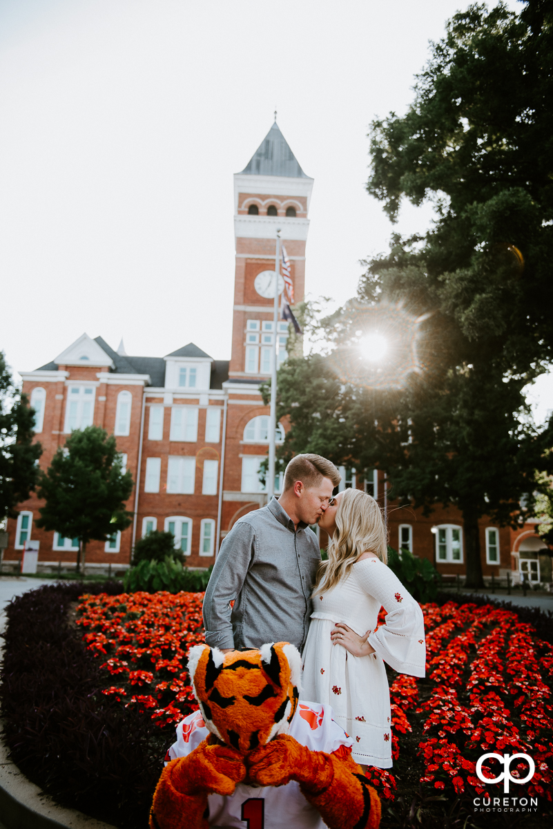 Engaged couple kissing in front of Tillman Hall while the Clemson Tiger Mascot covers his eyes.
