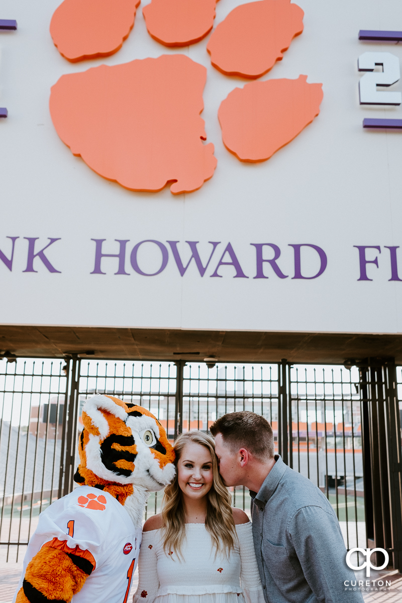 Woman being kissed on the cheek by both her fiancee and the Tiger mascot during an engagement session in Clemson,SC.