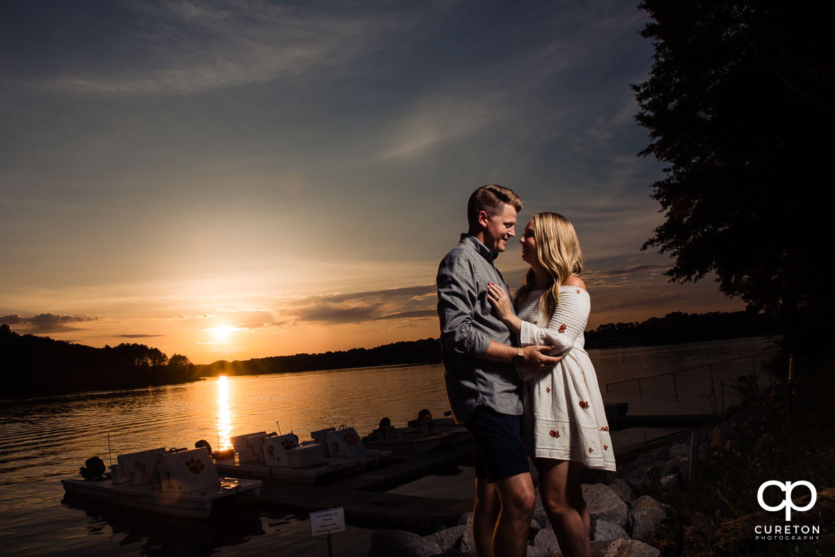 Engaged couple holding each other at sunset by the lake during a Clemson engagement session.