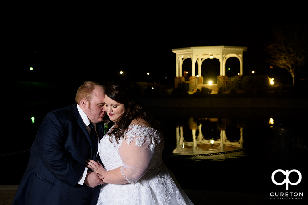 Bride and groom snuggling by the lake with reflections in the water.