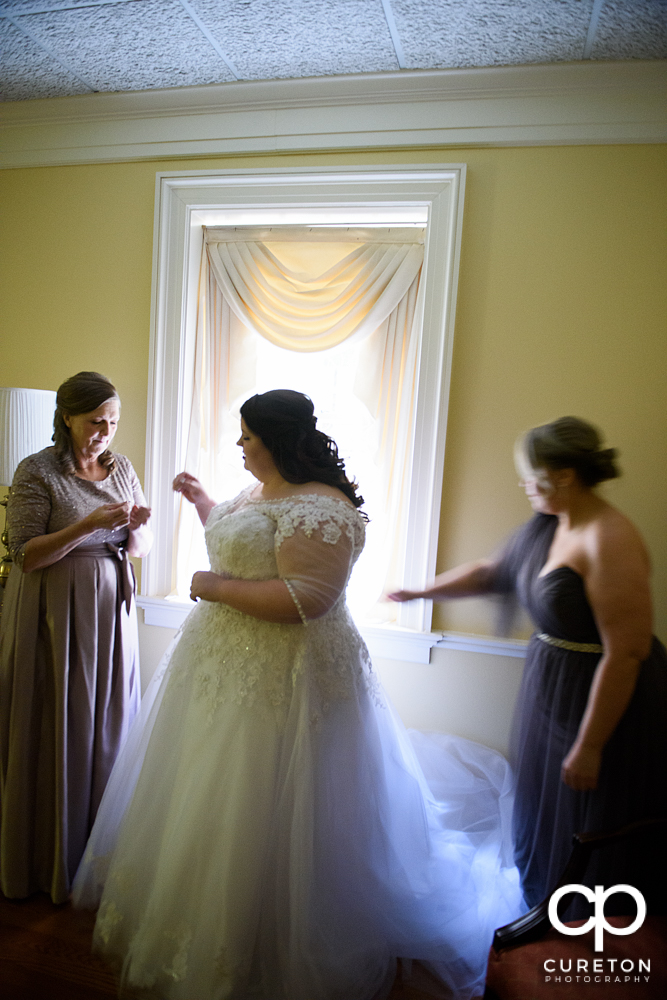 Bridesmaids helping the bride get into the dress.