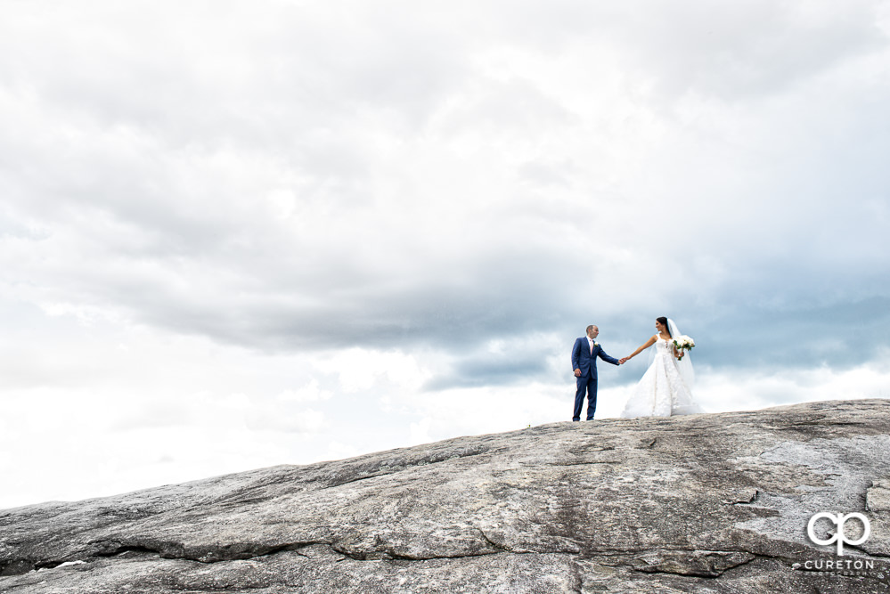 Bride and groom holding hands walking up a mountaintop after their Glassy Chapel wedding.