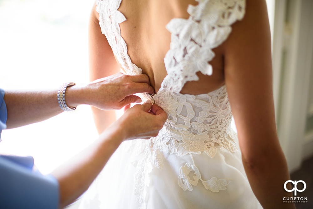 Bride's mother helping her zip the back of her wedding dress.