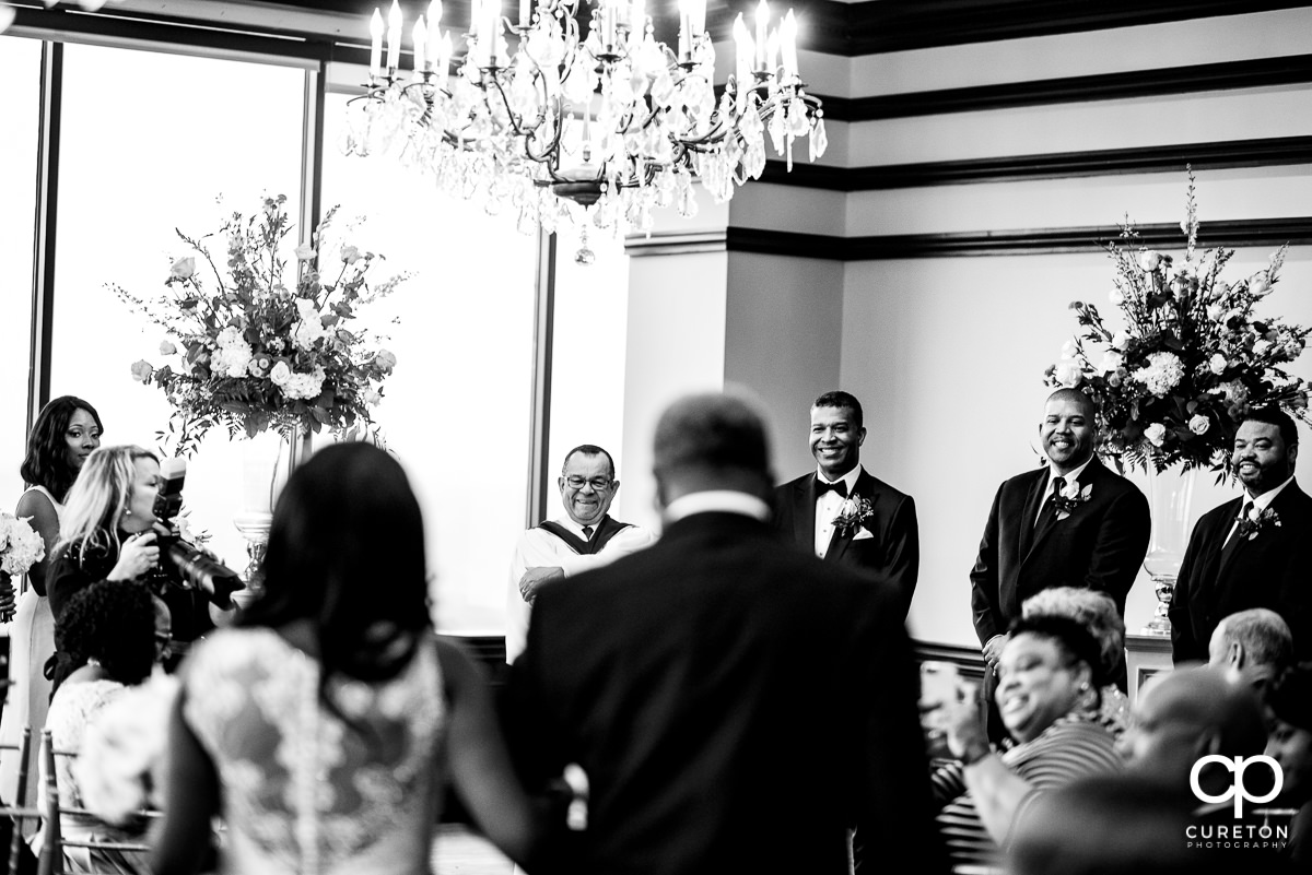Groom smiling as his bride is walked down the aisle by her father.