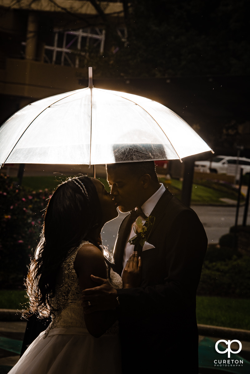 Bride and groom kissing underneath an umbrella outside in the rain in downtown Greenville,SC.