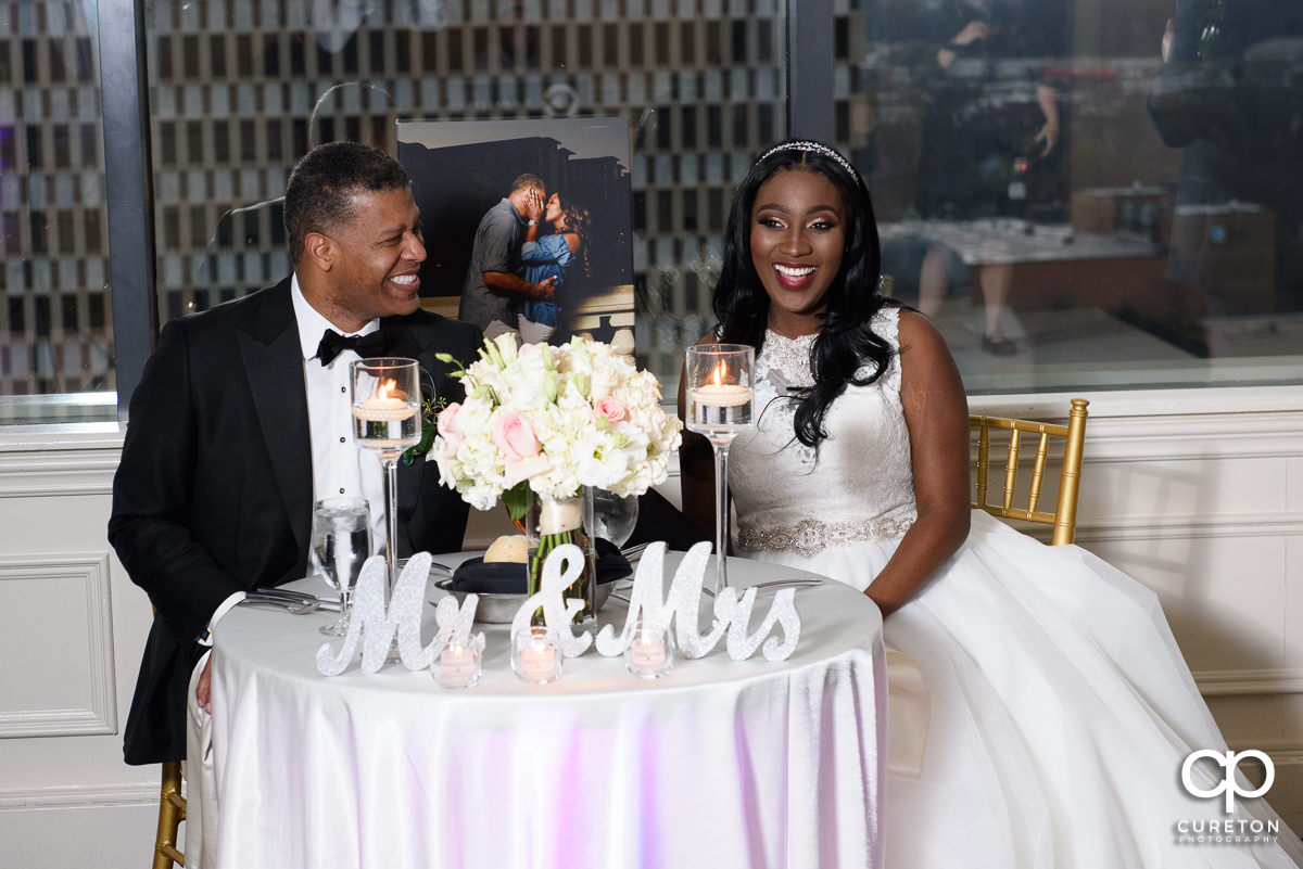 Newlywed couple laughing at the wedding speeches.