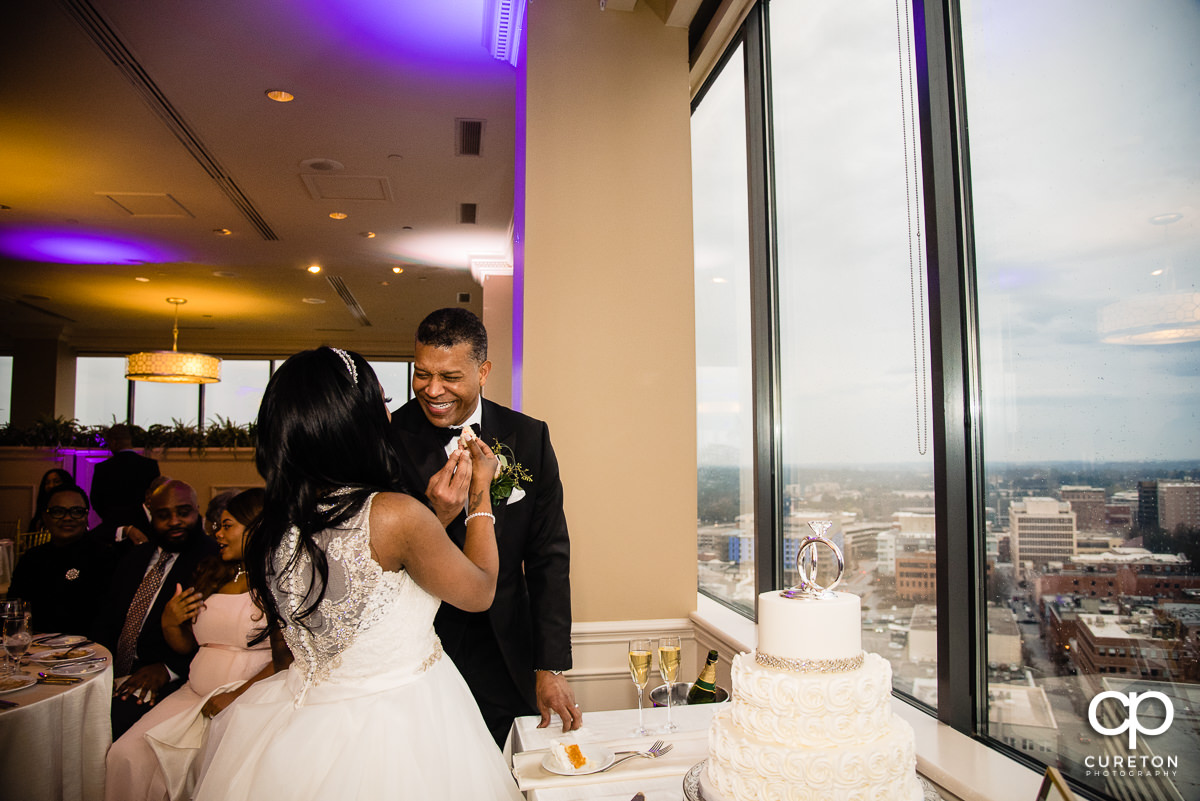 Bride and groom feeding cake to each other with a view of the Greenville skyline.