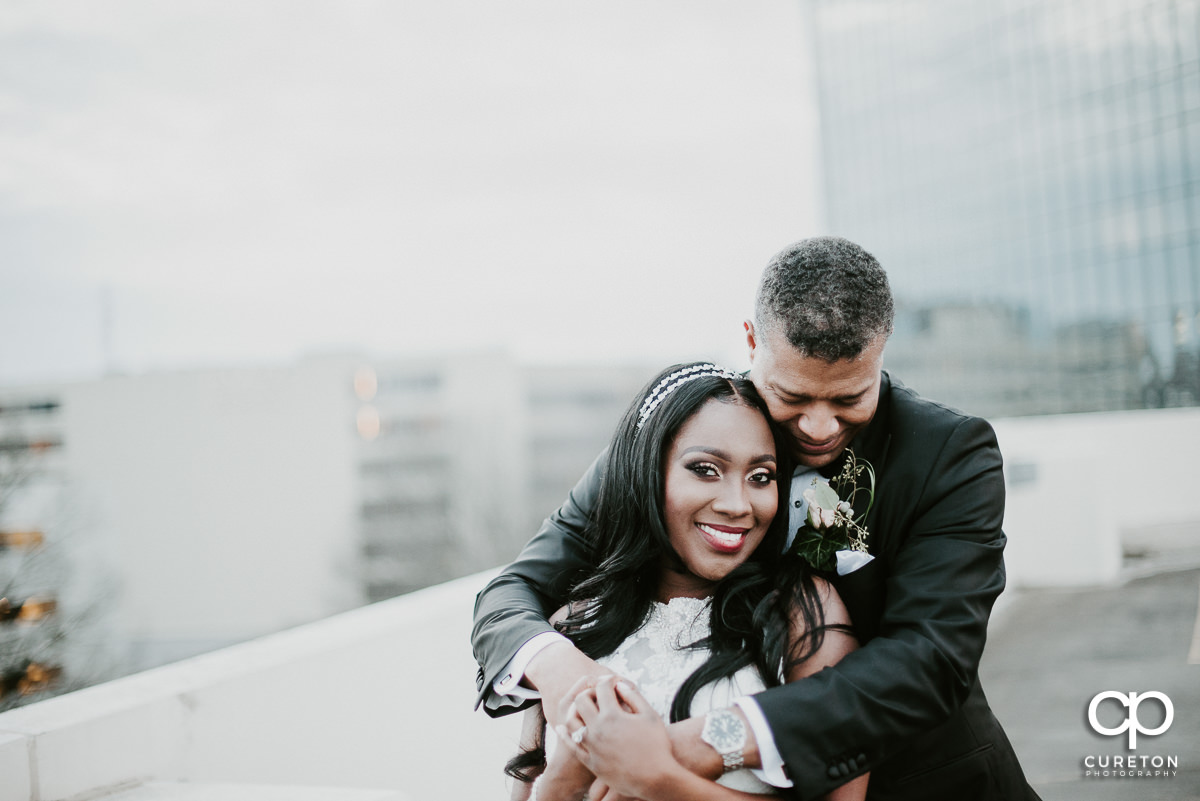 Groom hugging his bride on a rooftop.