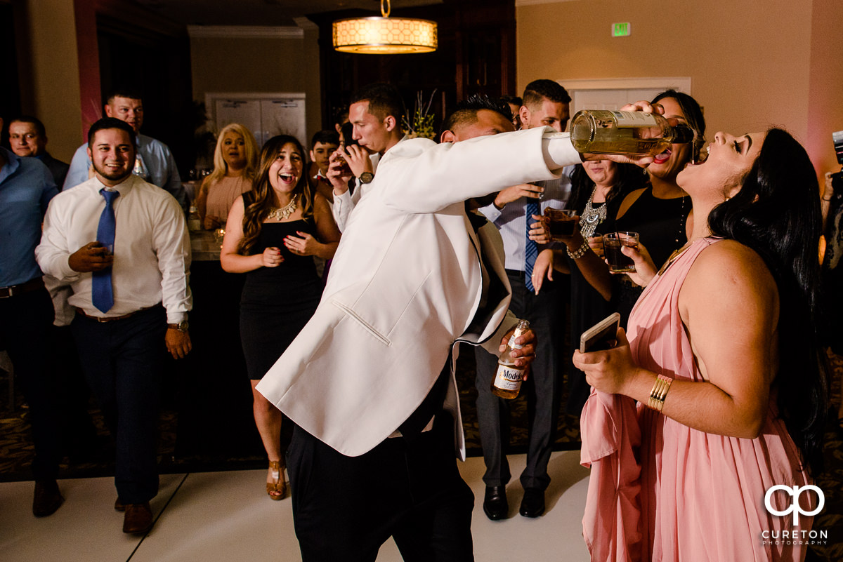 Groom pouring tequila into guests's mouths at the wedding reception.