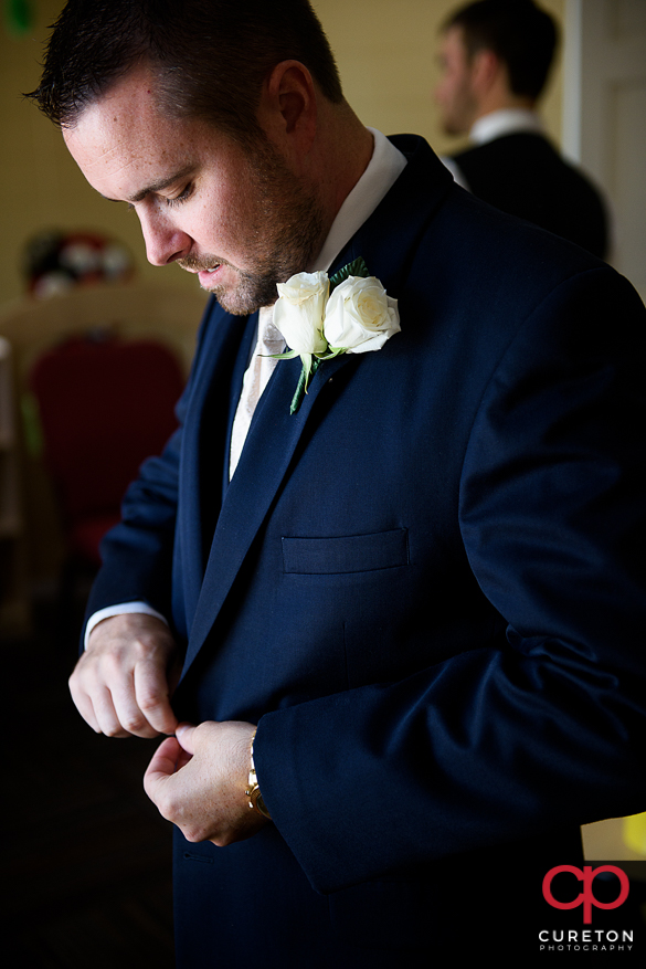 Groom fixing the buttons on his jacket.