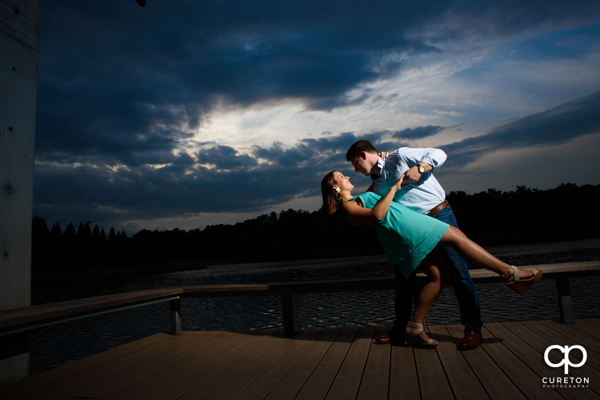 Groom dipping his future bride while dancing by the lake at sunset during a creative engagement session at Furman University in Greenville,SC.