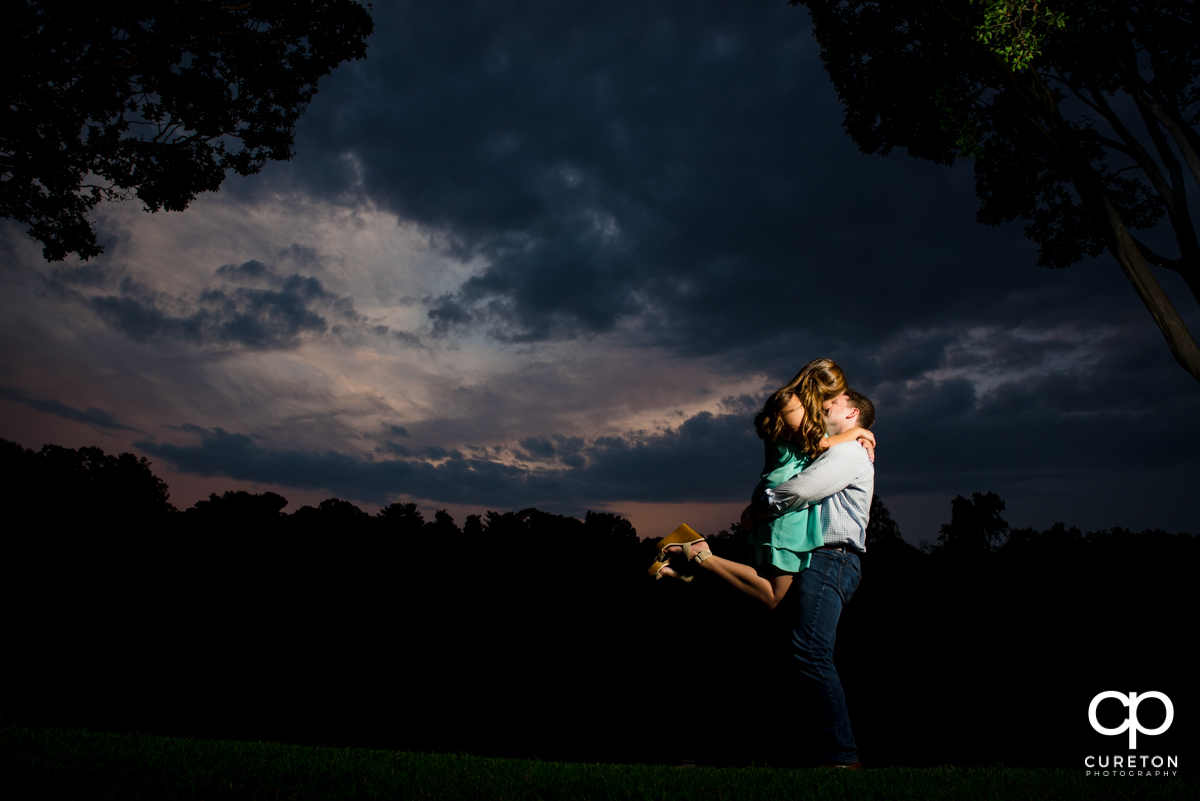 Man lifting his future bride by the lake during their sunset engagement session in Greenville,SC.