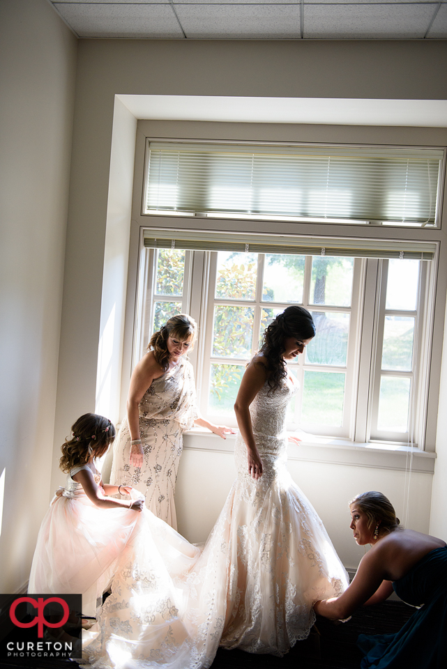 The bridesmaids help the bride into her dress.