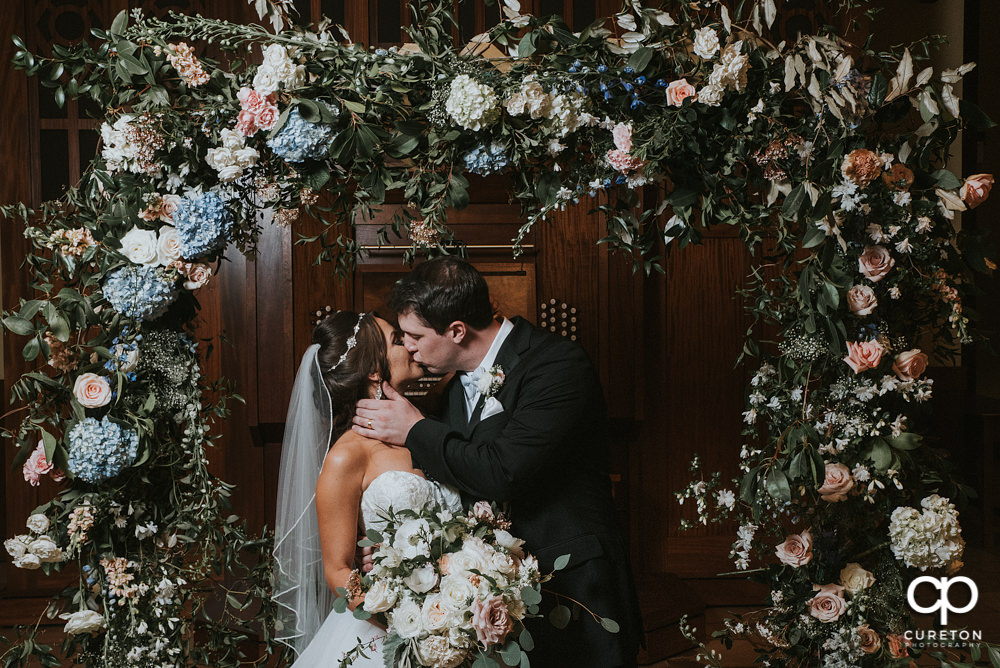 Bride and groom kissing in the middle of a gorgeous flower arch at Daniel Chapel at Furman university.