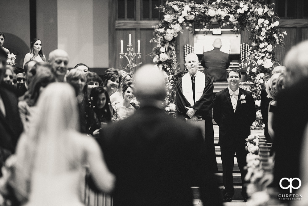 Groom smiling as he sees his bride for the first time walking down the aisle at Daniel Chapel.