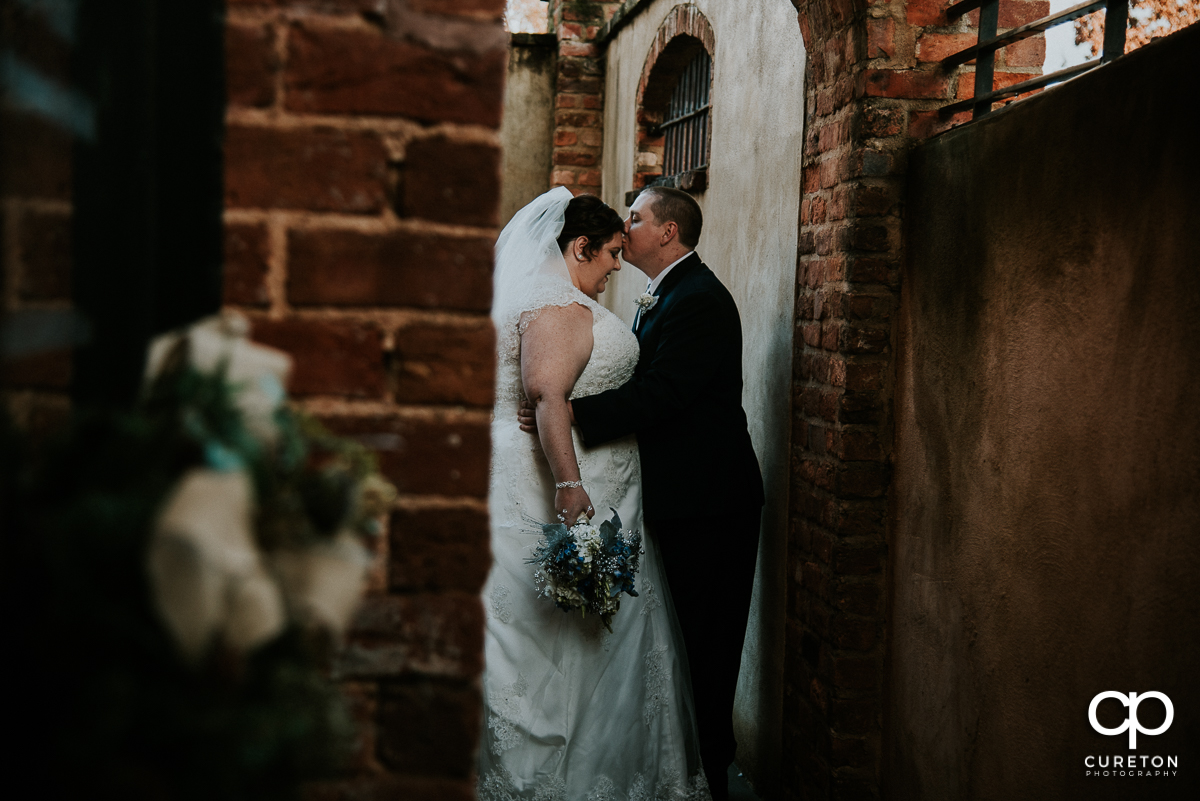 Groom kissing his bride on the forehead before their December Old Cigar Warehouse wedding in Greenville,SC.