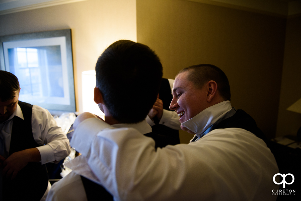 Groom helping his friend with a tie.