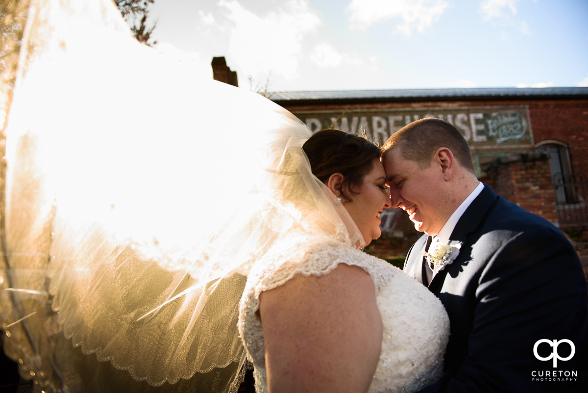 Bride hugging with her husband as her veil blows inth ewind and glowing sunlight at their December Old Cigar Warehouse wedding.