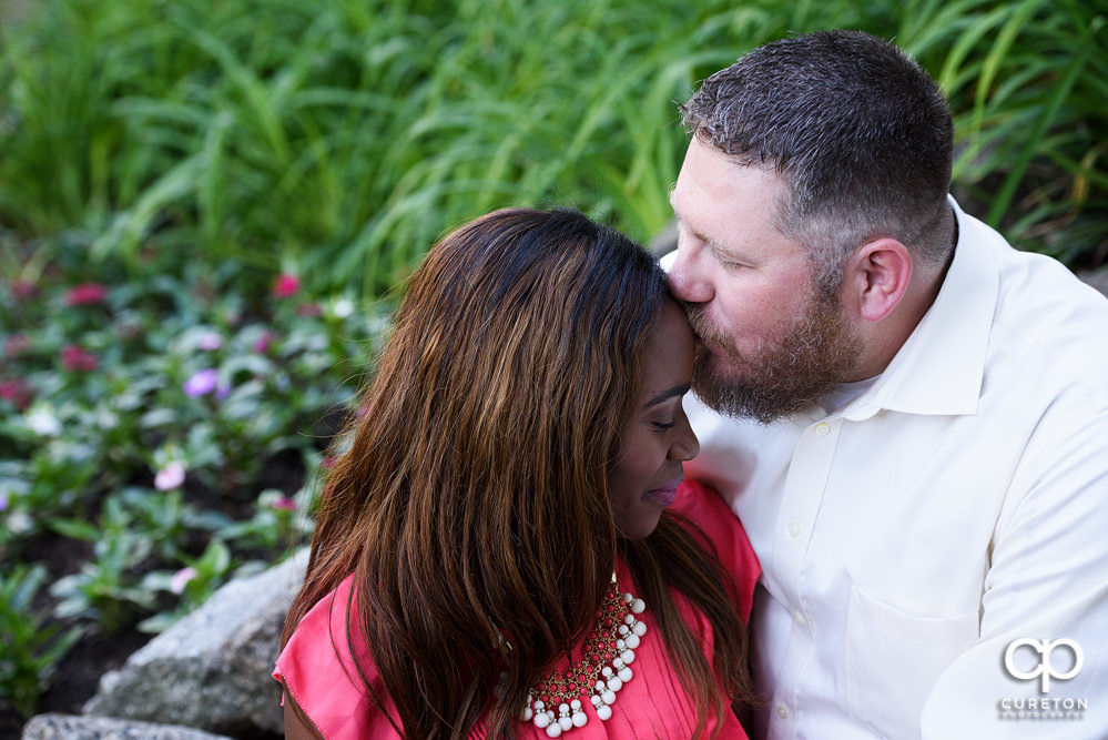 Groom kissing his bride on the forehead during their downtown Greenville park engagement session.