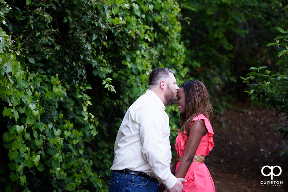Groom kissing his bride on the forehead during their downtown Greenville park engagement session.