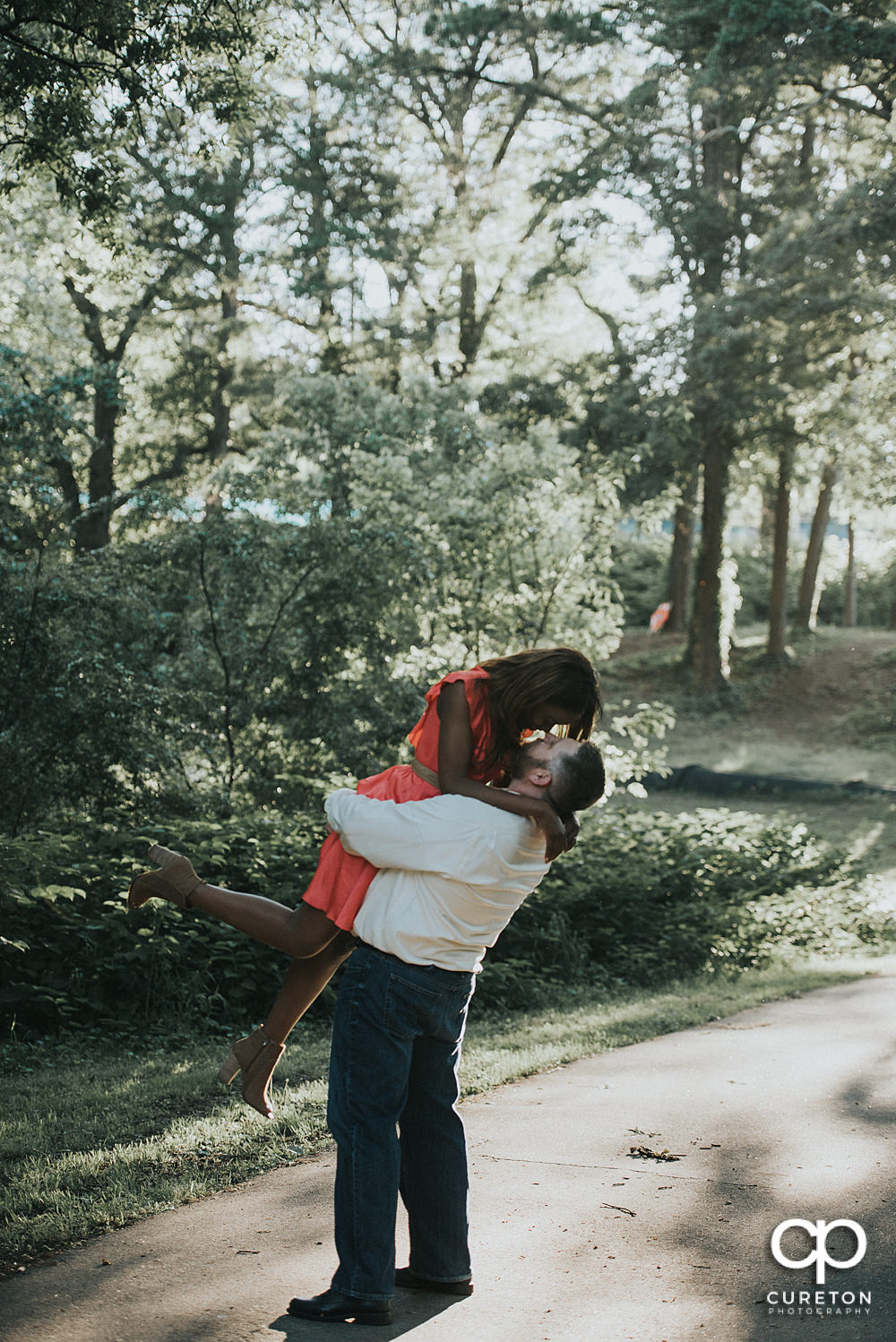 Bride being lifted by groom in the park.