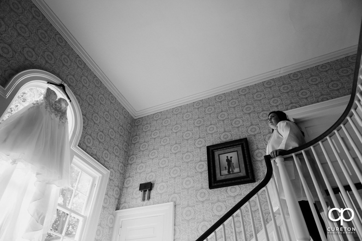 Bride standing on the stairs at Duncan Estate looking at her dress hanging in the window.