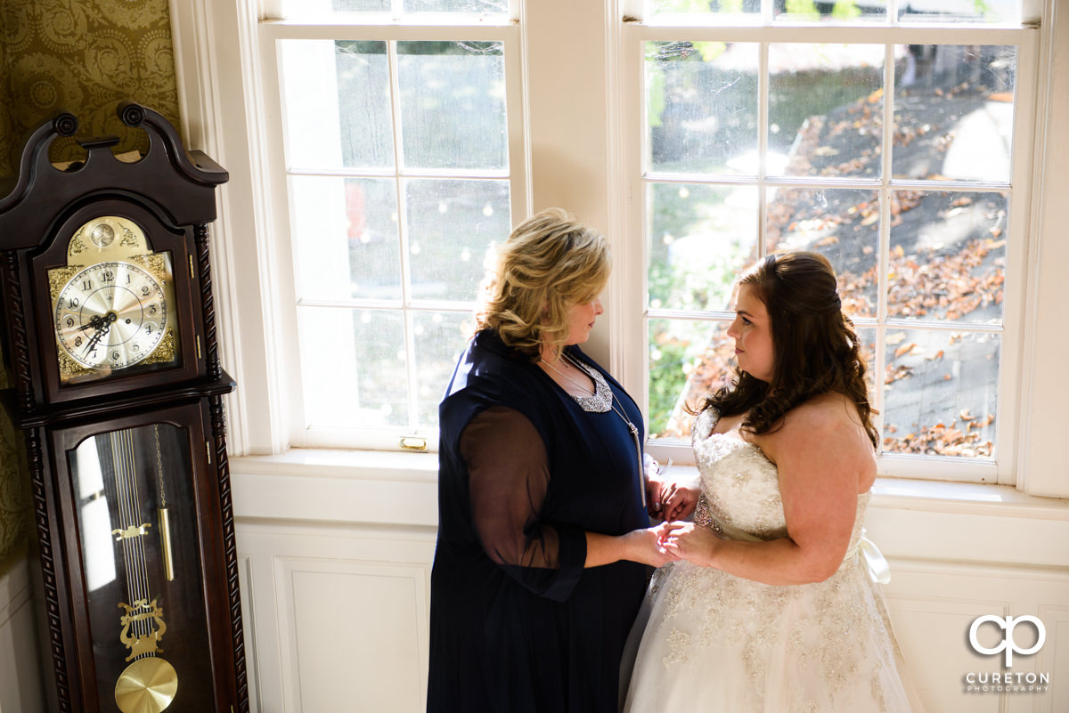Bride and her mom standing in front of a window sharing a moment before the wedding.
