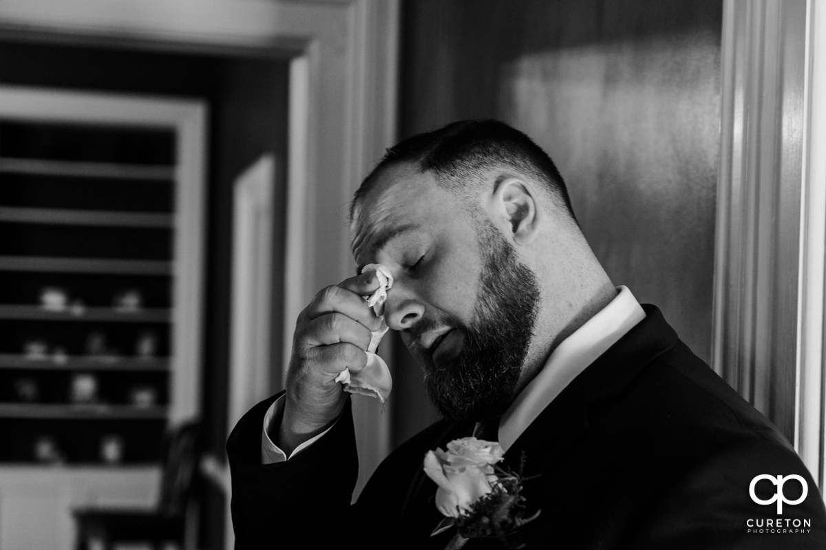 Groom wiping away tears after praying with his bride before the wedding.