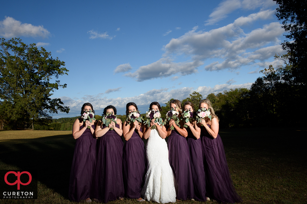 Bride and bridesmaids with their flowers over their faces.