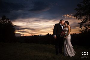 Bride and groom kissing in a field at sunset.