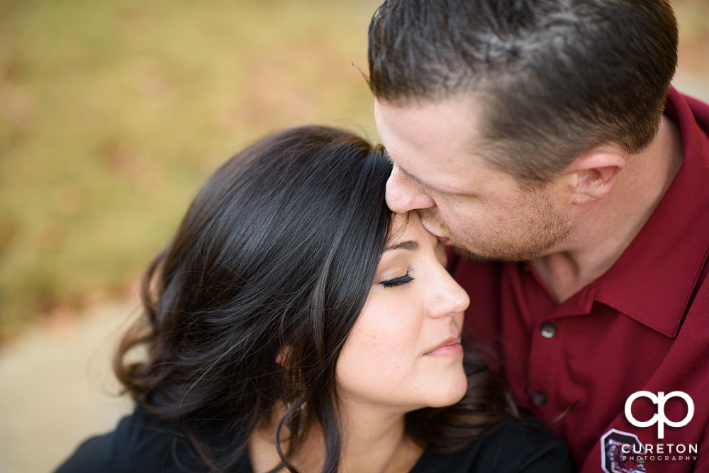 Groom kissing his bride on the forehead during their engagement session at Furman university.