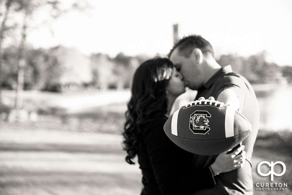 Bride and groom kissing while the groom is holding a football.