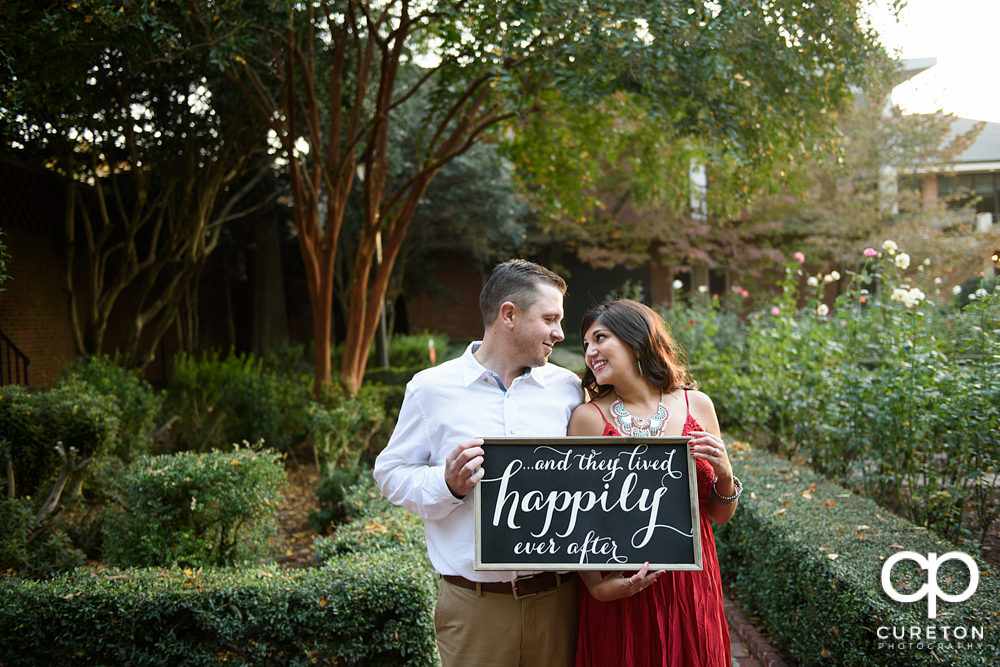 Couple holding a sign in the rose garden during their Furman university engagement session.
