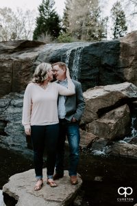 Engaged couple cuddling on a rock near a waterfall indowntwon Greenville,SC.