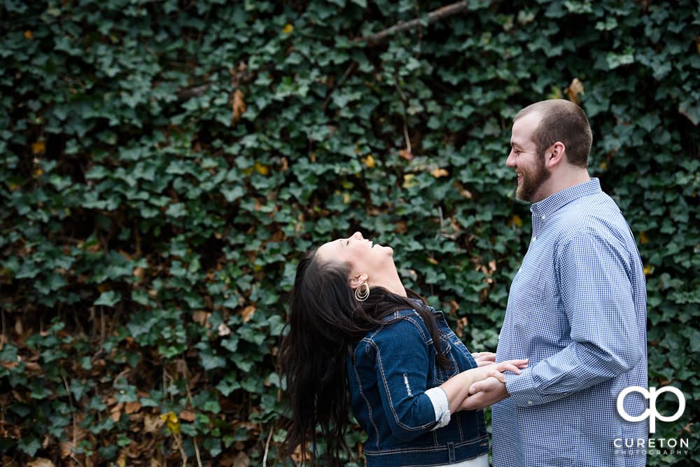 Couple laughing in front of a wall of ivy during their engagement session in Falls Park.