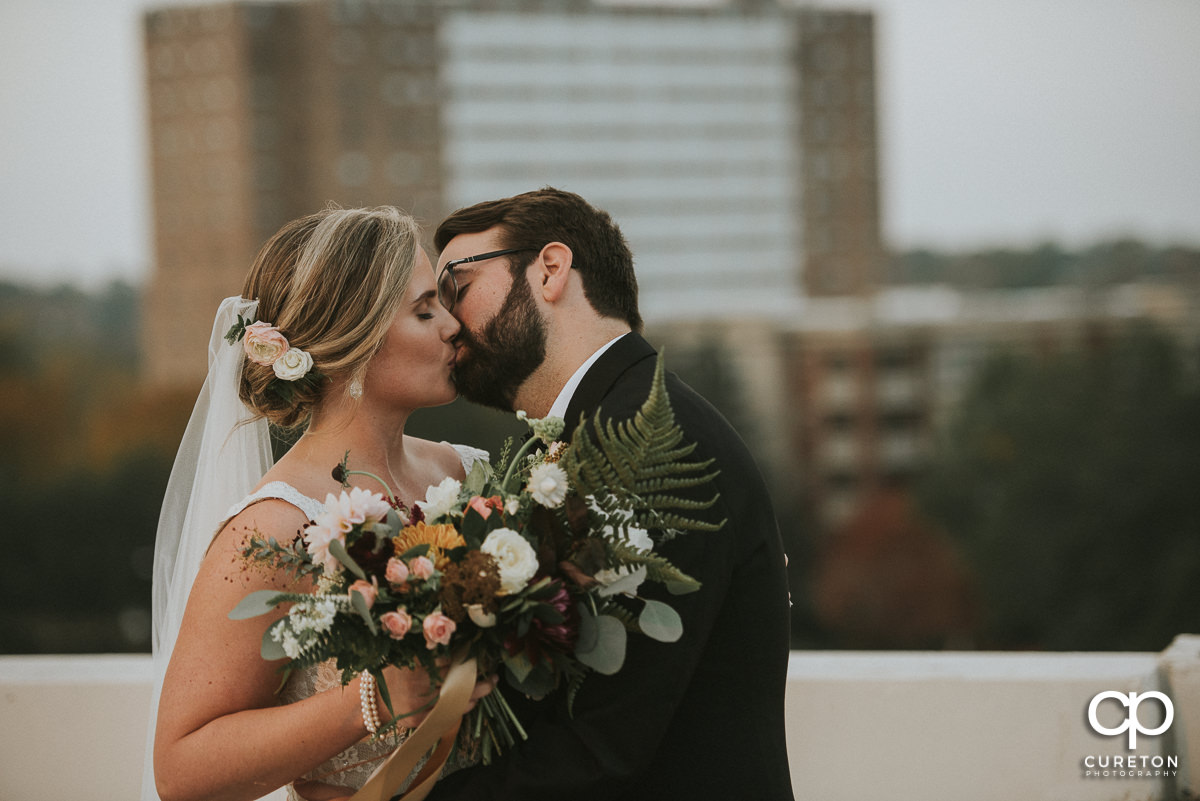 Bride and groom kissing on a rooftop.