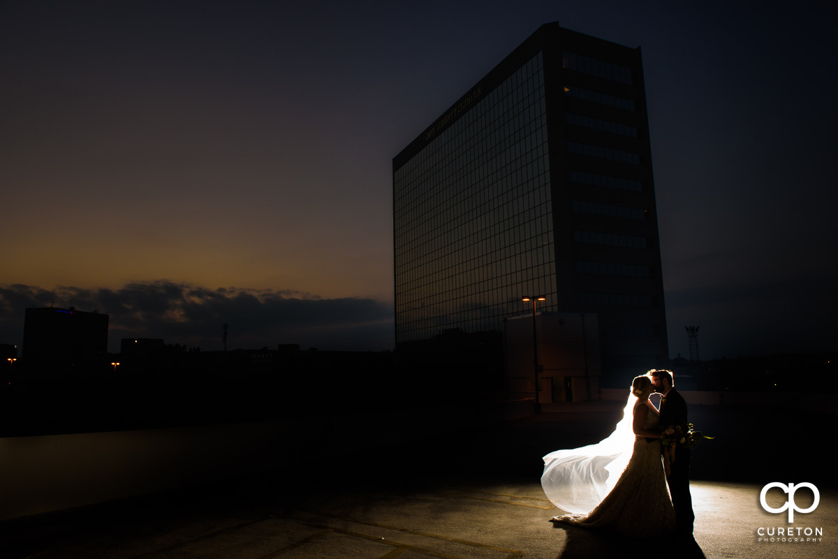 Bride and groom kissing on a rooftop at sunset with the downtown Greenville skyline in the background at their Commerce Club wedding.
