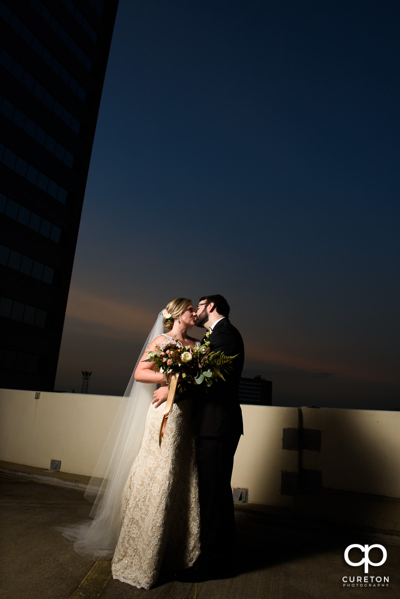 Married couple kissing on the roof in downtown Greenville at the Commerce Club during their wedding reception.