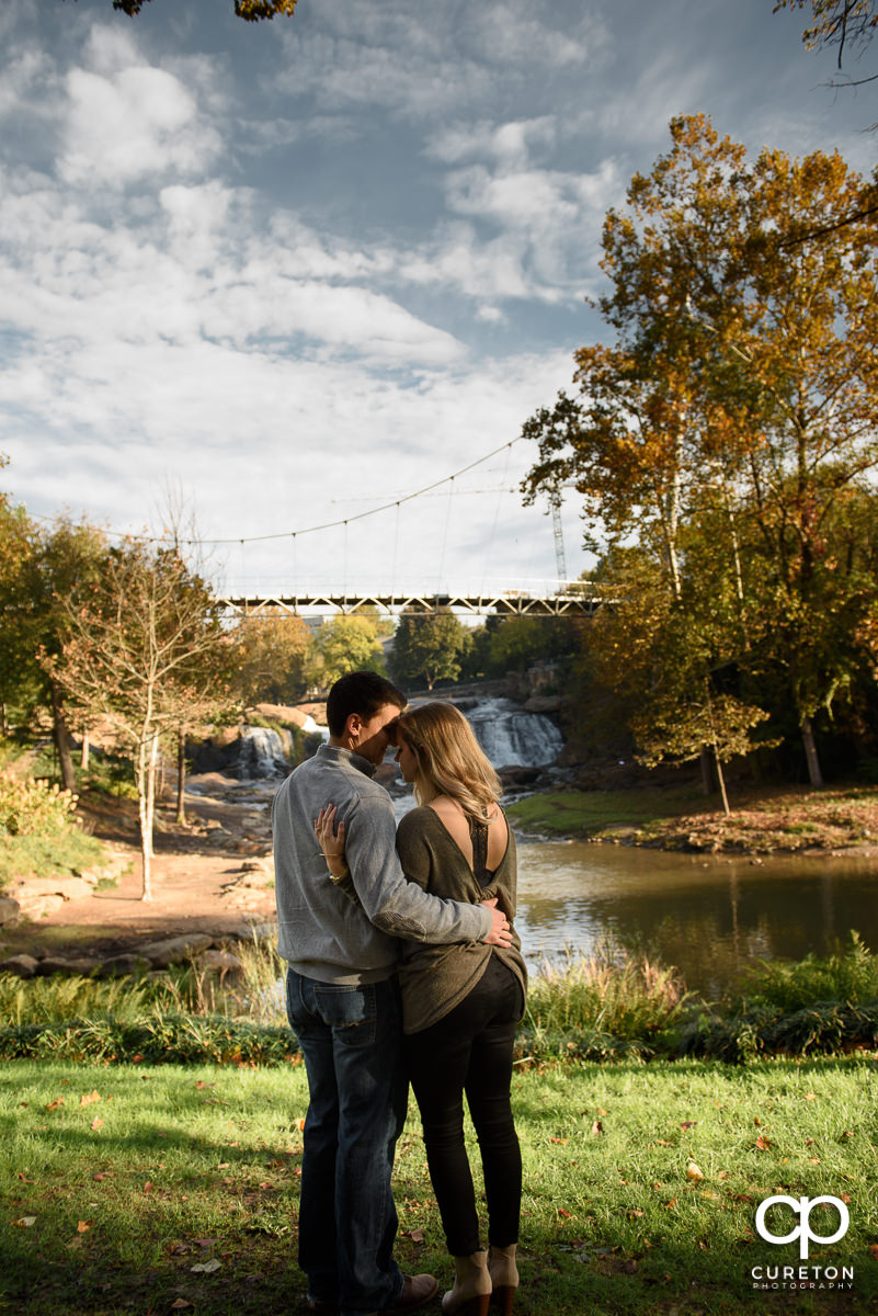 Bride and groom hugging with Liberty Bridge in the background during an engagement session in Greenville,SC.